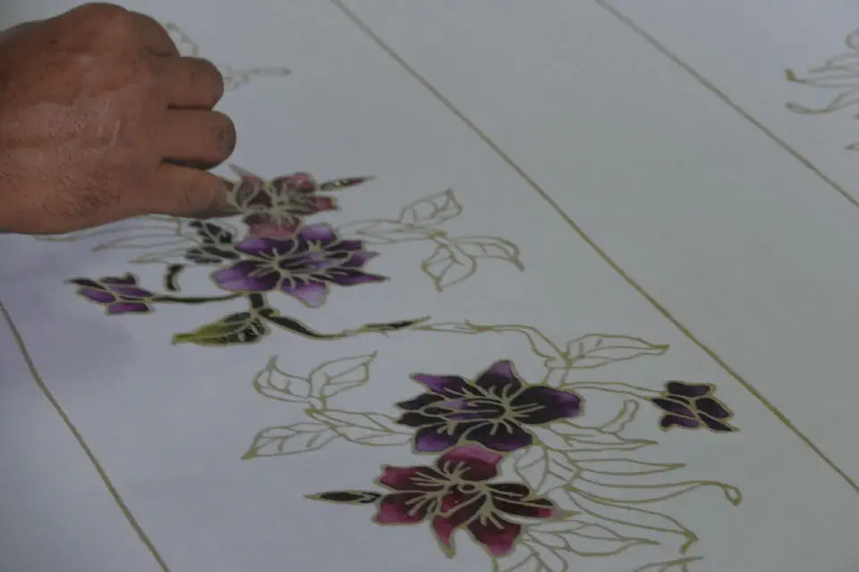 An artisan carefully paints the floral patterns by hand.